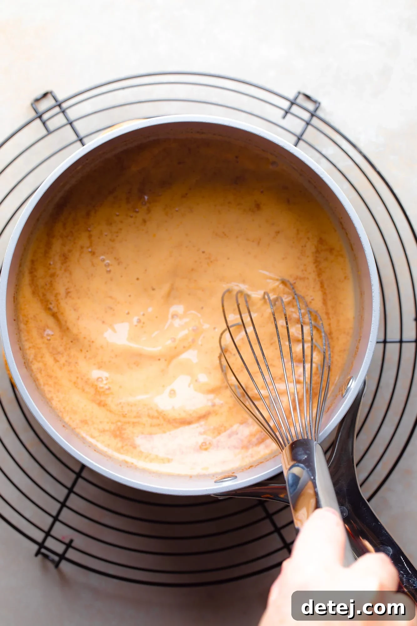 A grey pot on the stove, containing a creamy orange pumpkin mixture, actively being whisked to combine the ingredients smoothly.