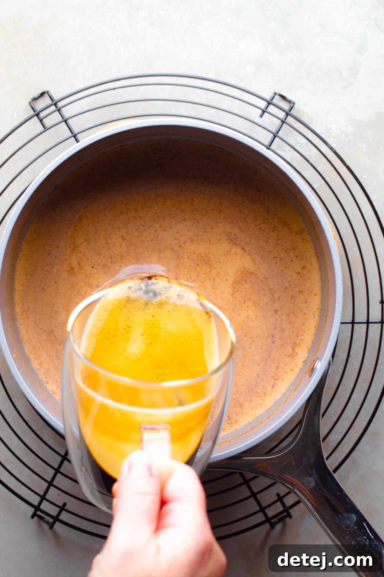A stream of rich, dark espresso being poured into a pot containing the creamy orange milk mixture, illustrating the final step of combining the latte components.