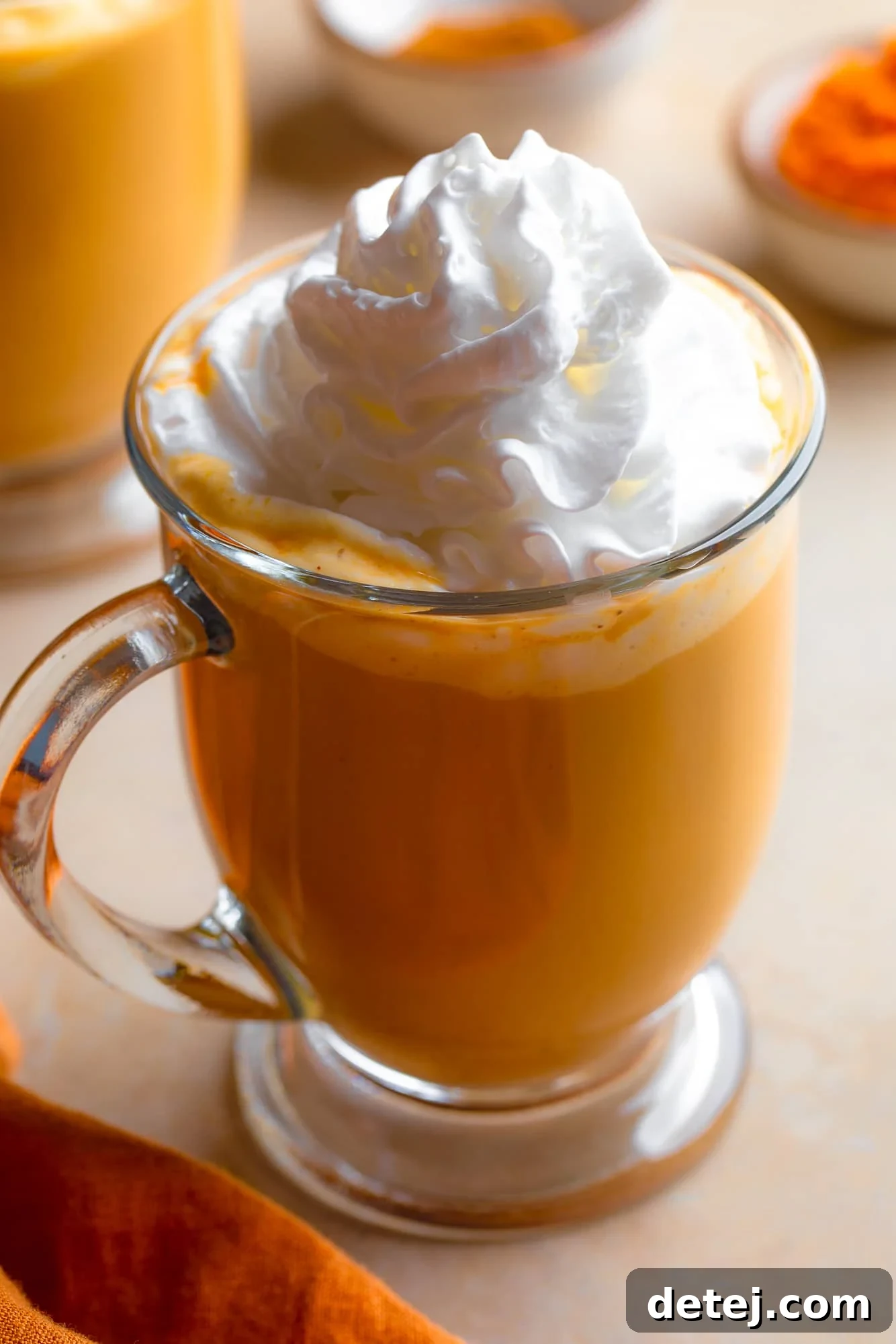 A vibrant glass mug holding a freshly made vegan pumpkin spice latte, adorned with a delicate layer of dairy-free whipped cream, capturing the essence of autumnal indulgence.