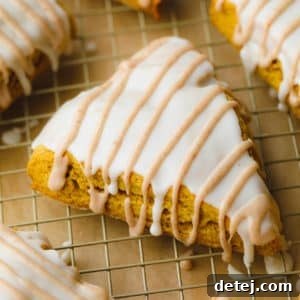 A single triangular vegan pumpkin scone with distinct white and tan glazes, resting on a cooling rack.