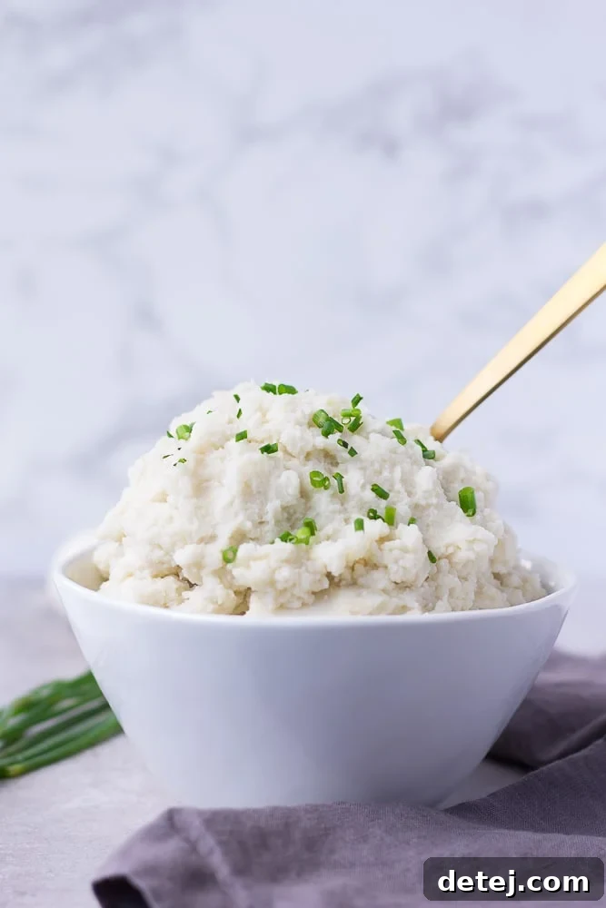A side view of a bowl of creamy vegan mashed potatoes, presented against a soft gray background, emphasizing its smooth texture.