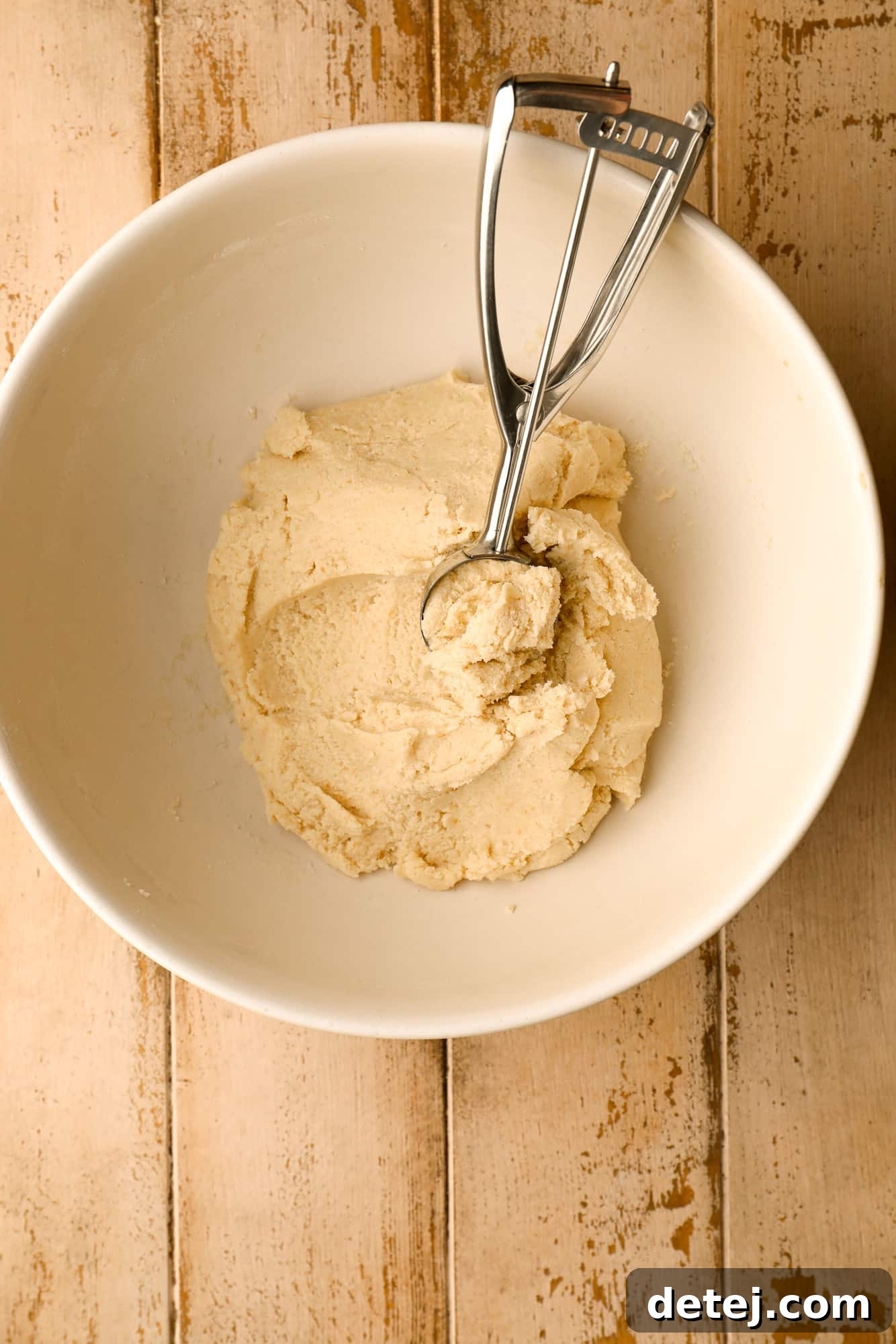 A cookie scoop efficiently scooping soft white cookie dough from a bowl, ready for rolling.