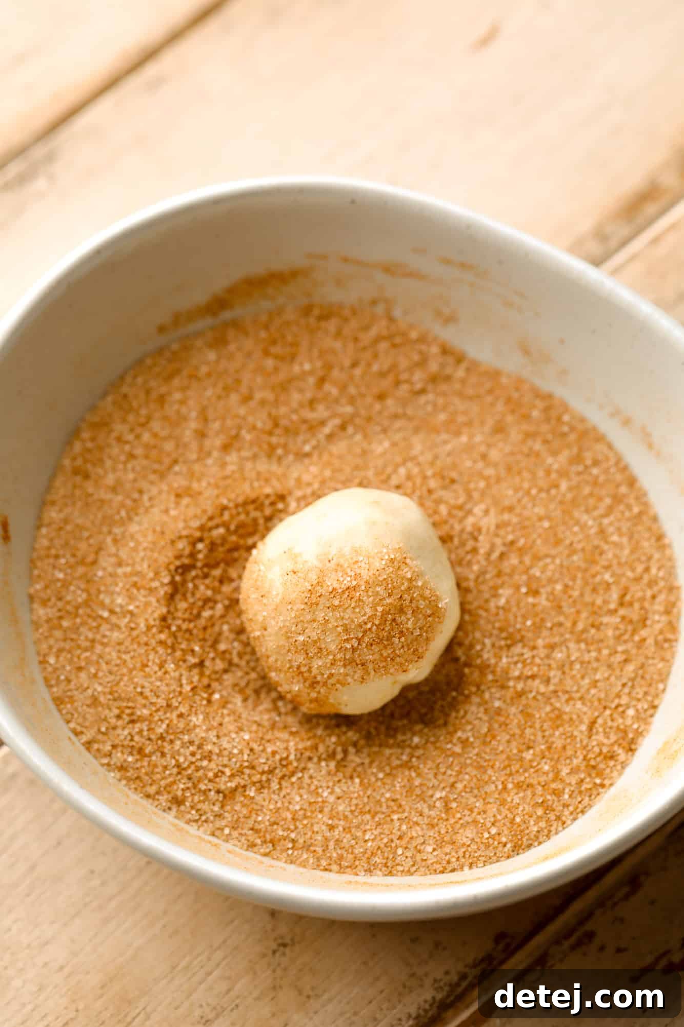 A hand gently rolling a cookie dough ball in a bowl filled with fragrant cinnamon sugar, ensuring full coverage.