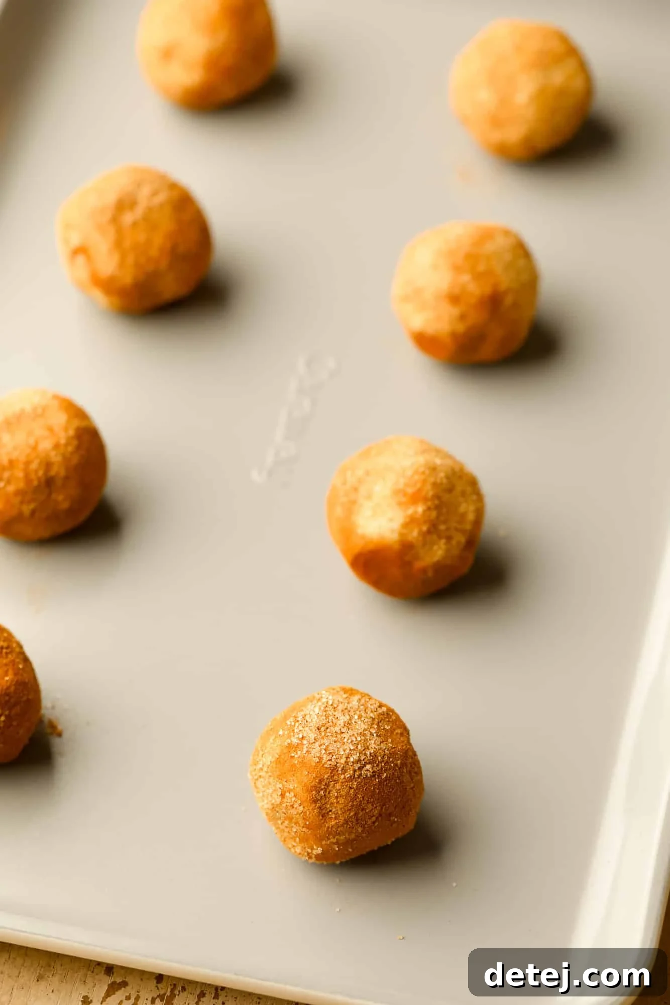 Rows of perfectly coated cinnamon-sugar cookie dough balls arranged on a metal baking sheet, ready for the oven.