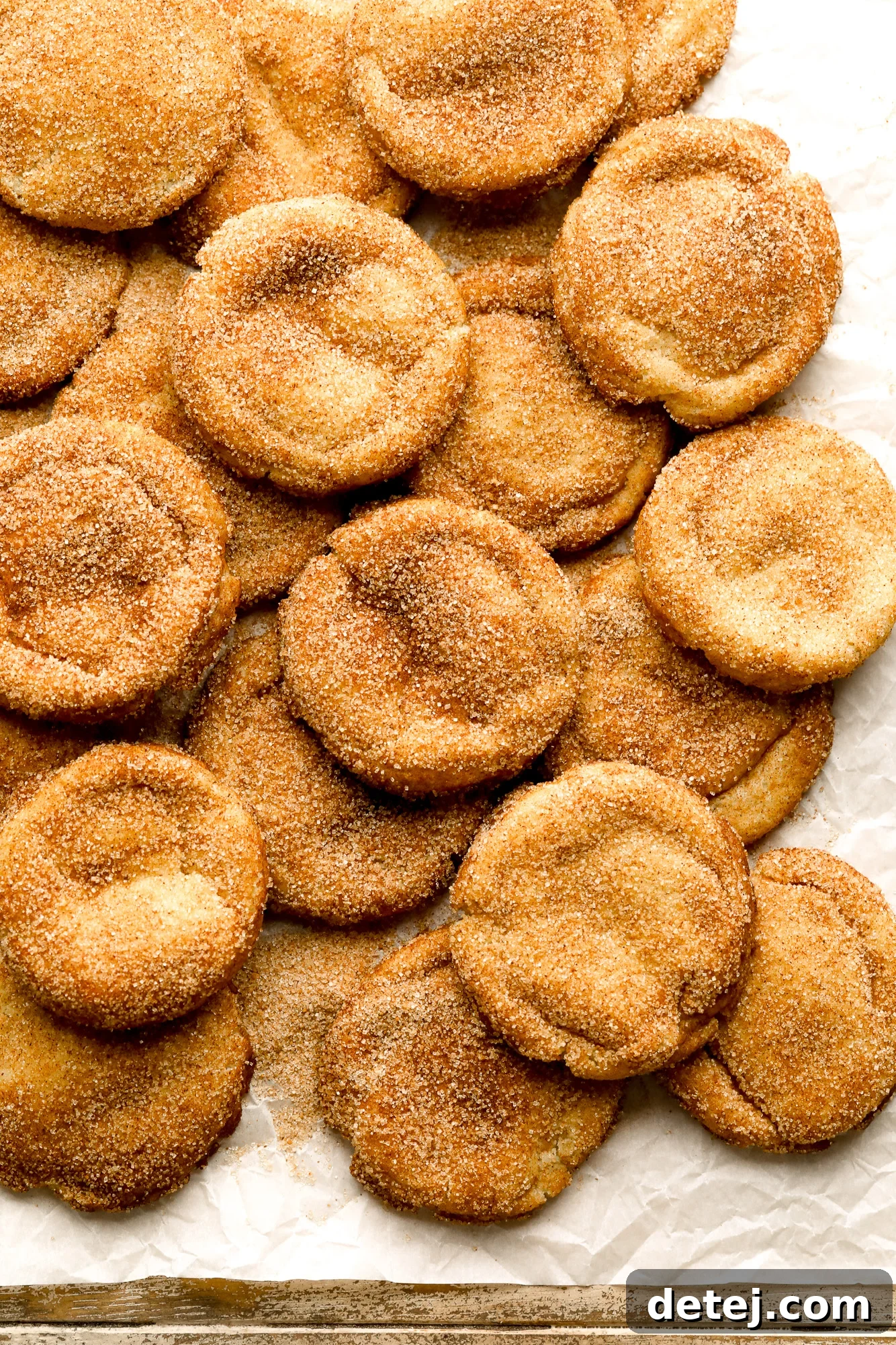 A generous pile of freshly baked vegan snickerdoodles resting on a piece of parchment paper, showcasing their perfect texture.