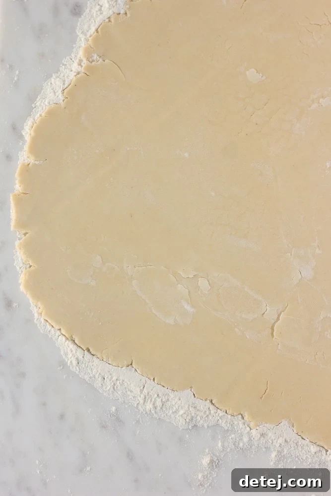 Vegan pie crust being carefully rolled out on a lightly floured surface with a rolling pin.