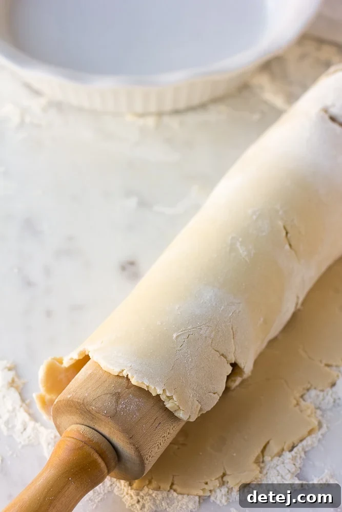 Vegan pie crust delicately draped over a rolling pin, ready to be transferred to a pie dish.
