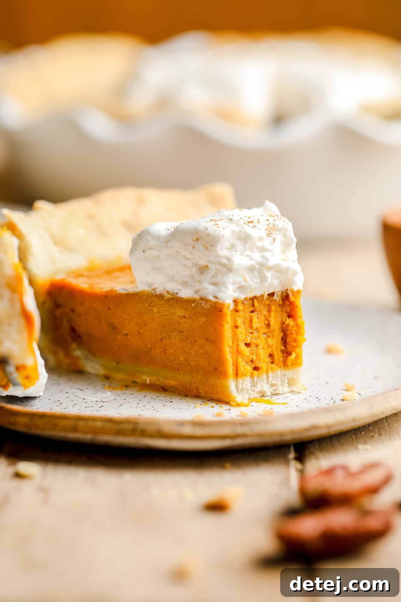 A perfectly sliced piece of vegan pumpkin pie, showcasing its smooth, creamy filling and golden crust, topped with a dollop of fluffy vegan whipped cream. A small bite has been taken, revealing the luxurious texture.