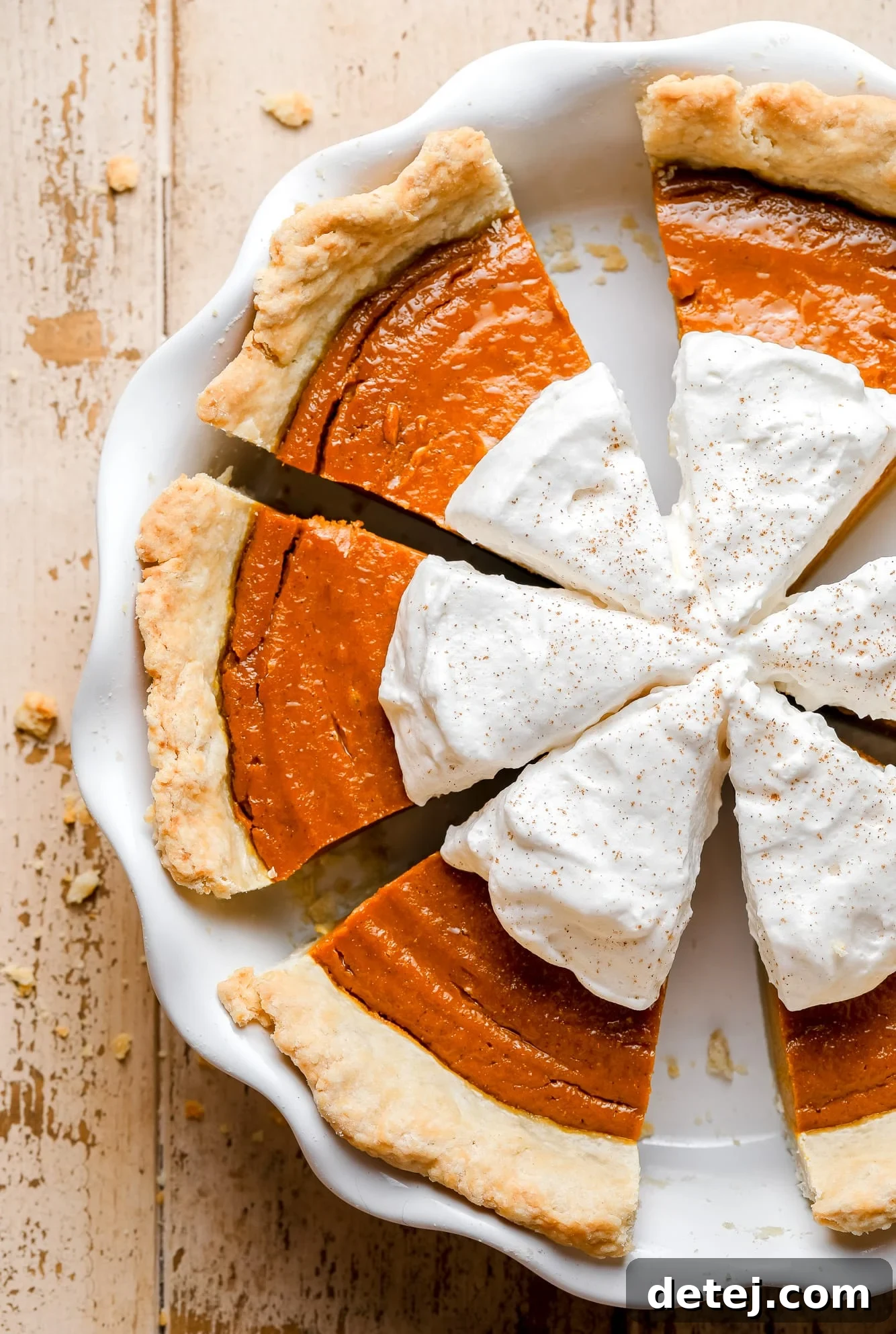 A close-up view of a whole vegan pumpkin pie in a white pie dish, elegantly sliced and topped with generous swirls of vegan whipped cream, ready to be served.