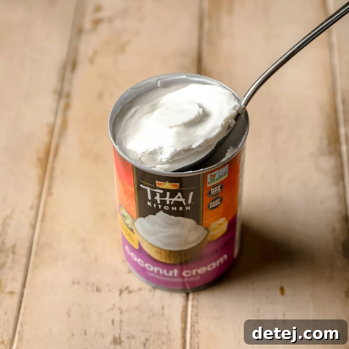 A spoon carefully removing a generous scoop of thick, white coconut cream from a can, highlighting its rich texture.