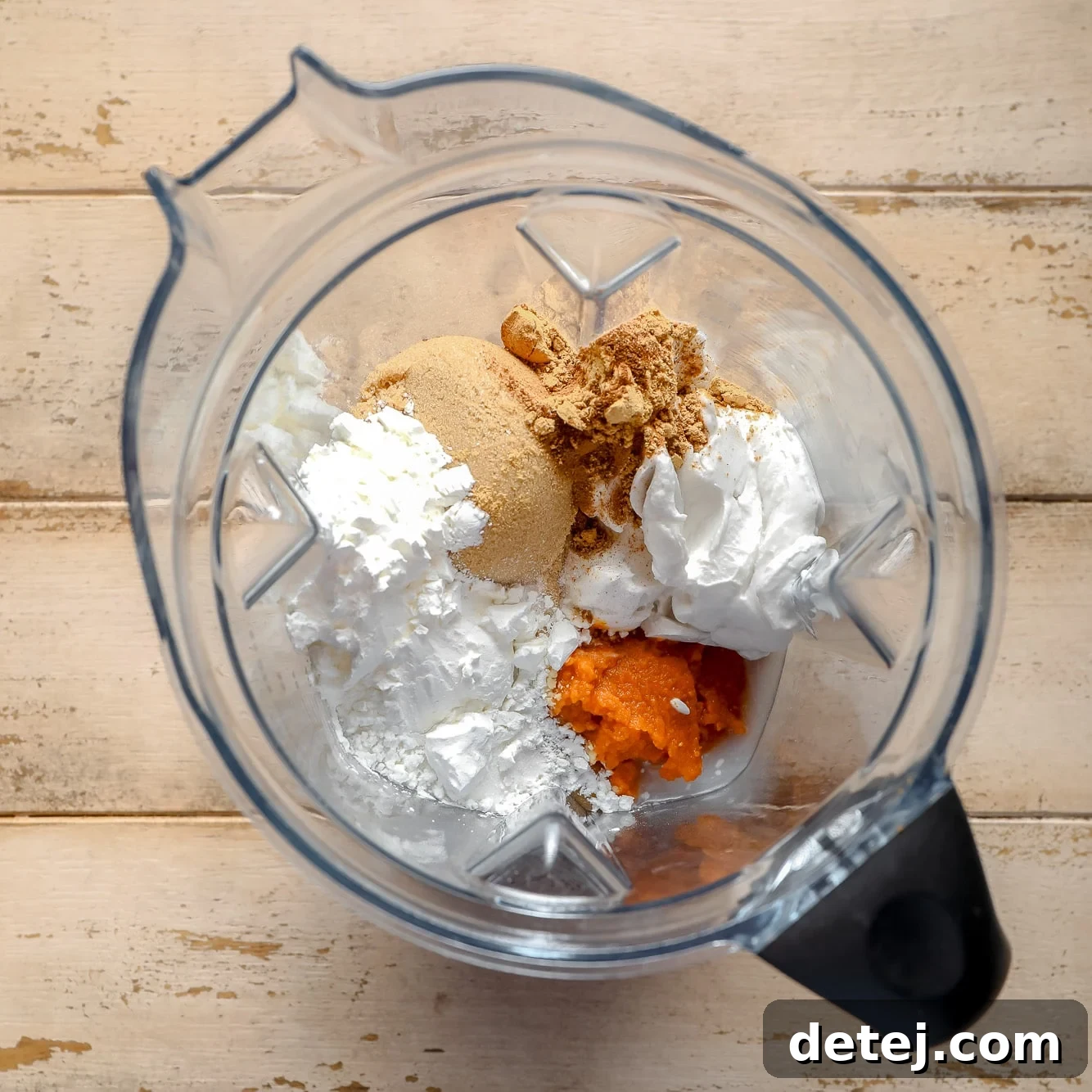 All the pumpkin pie filling ingredients, including canned pumpkin, spices, and coconut cream, gathered inside a blender jug, ready for blending.