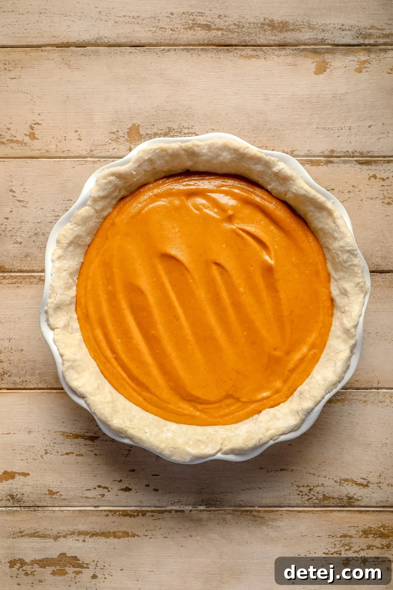 An unbaked vegan pumpkin pie in a pristine white pie dish, showcasing the smooth, unbaked filling settled within the crust, ready for the oven.
