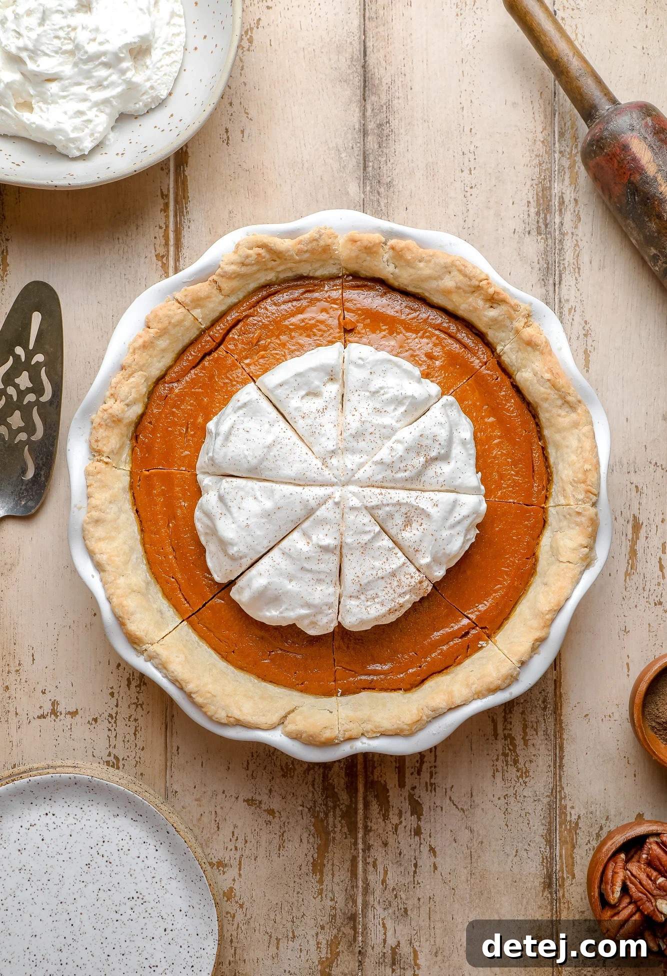 A beautifully decorated vegan pumpkin pie, generously topped with fluffy white whipped cream, nestled in a white pie dish, ready to be enjoyed.