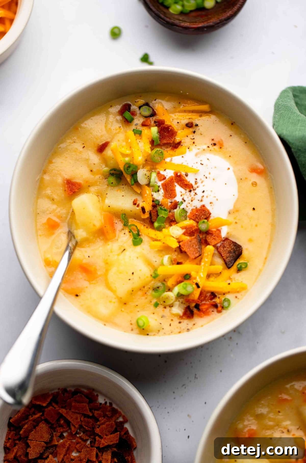 looking down on a bowl of vegan potato soup with toppings on white backdrop