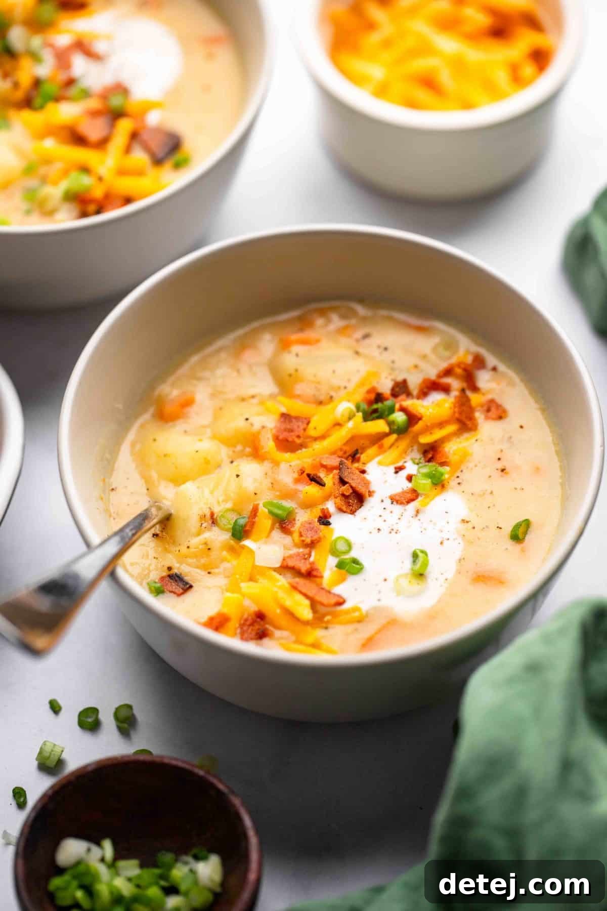 vegan potato soup in cream colored bowl with sour cream and bacon for toppings