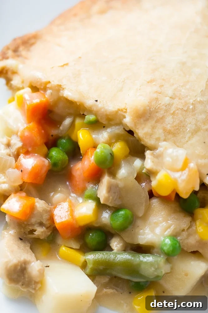 Close-up of a slice of vegan pot pie, revealing the creamy filling and flaky golden crust, garnished with fresh herbs.
