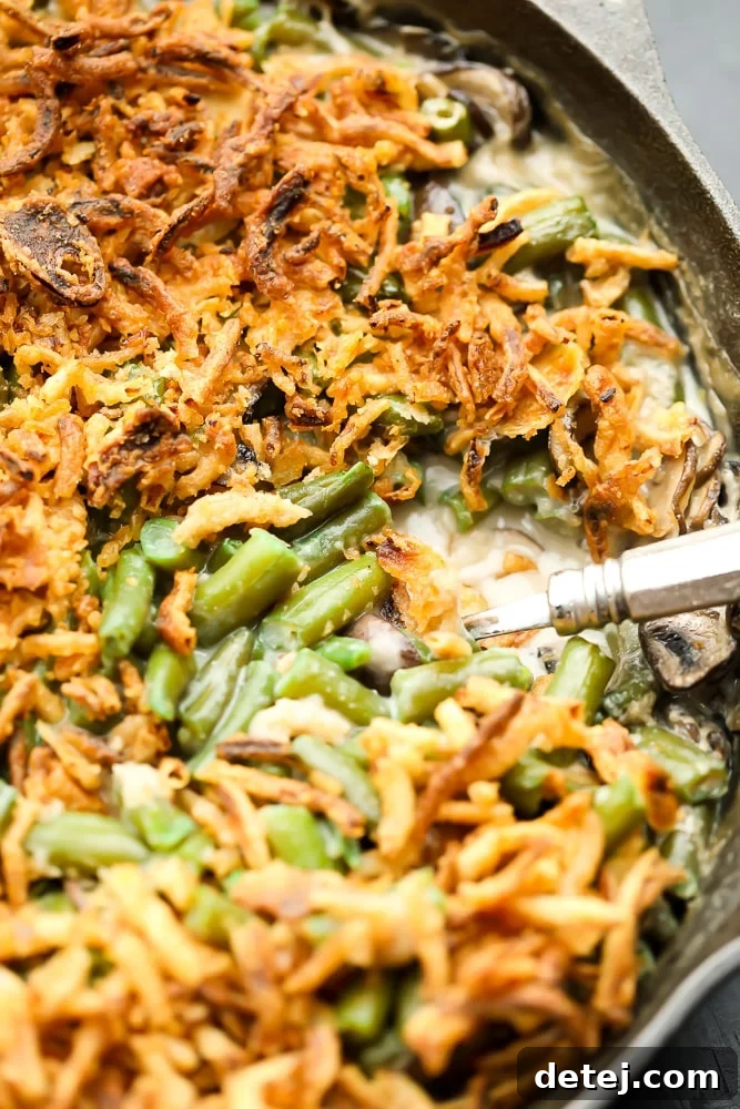 Close up of a spoonful of creamy vegan green bean casserole with crispy onions in a black pan, showing texture.