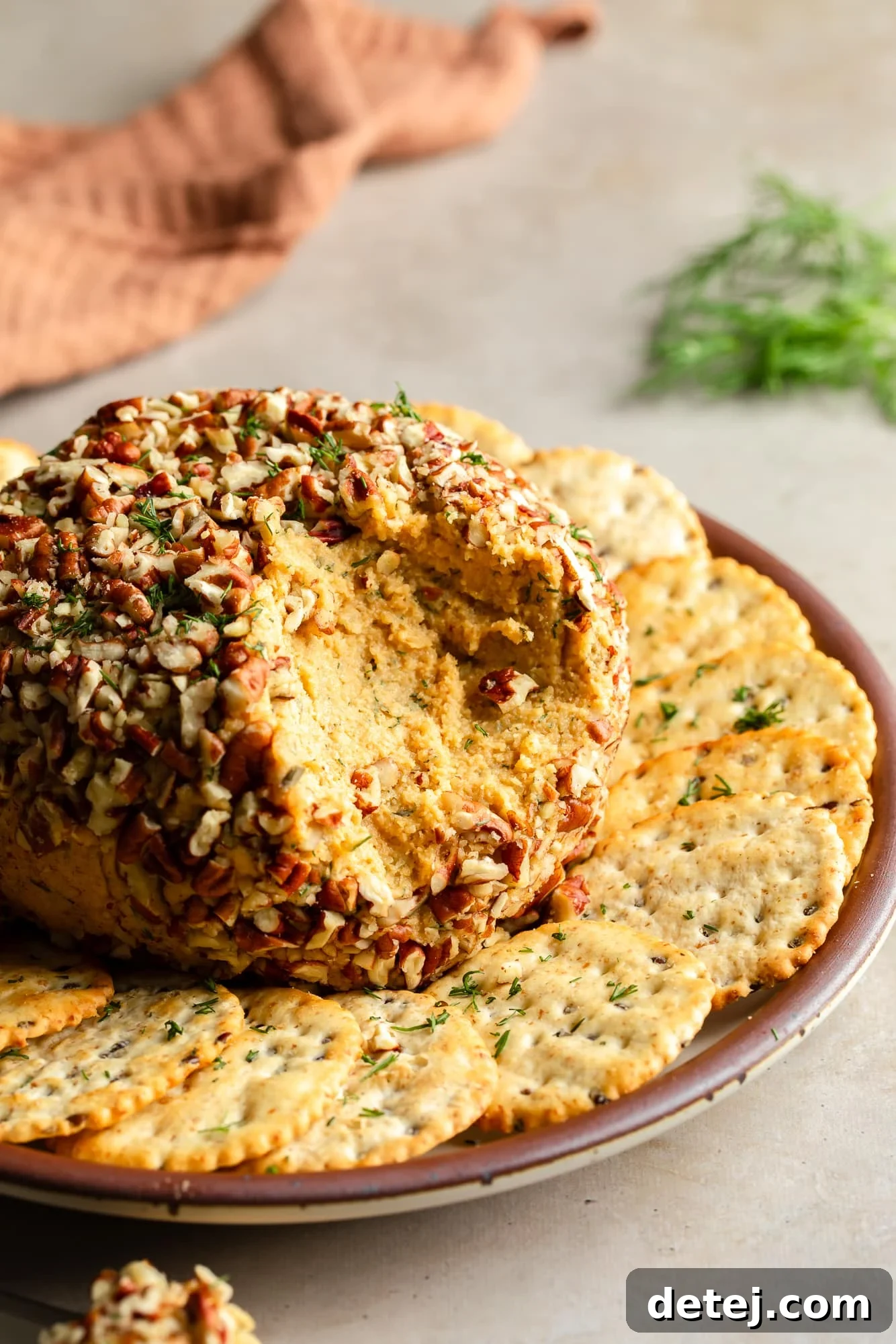a vegan cheese ball with scoop missing on a plate with crackers.