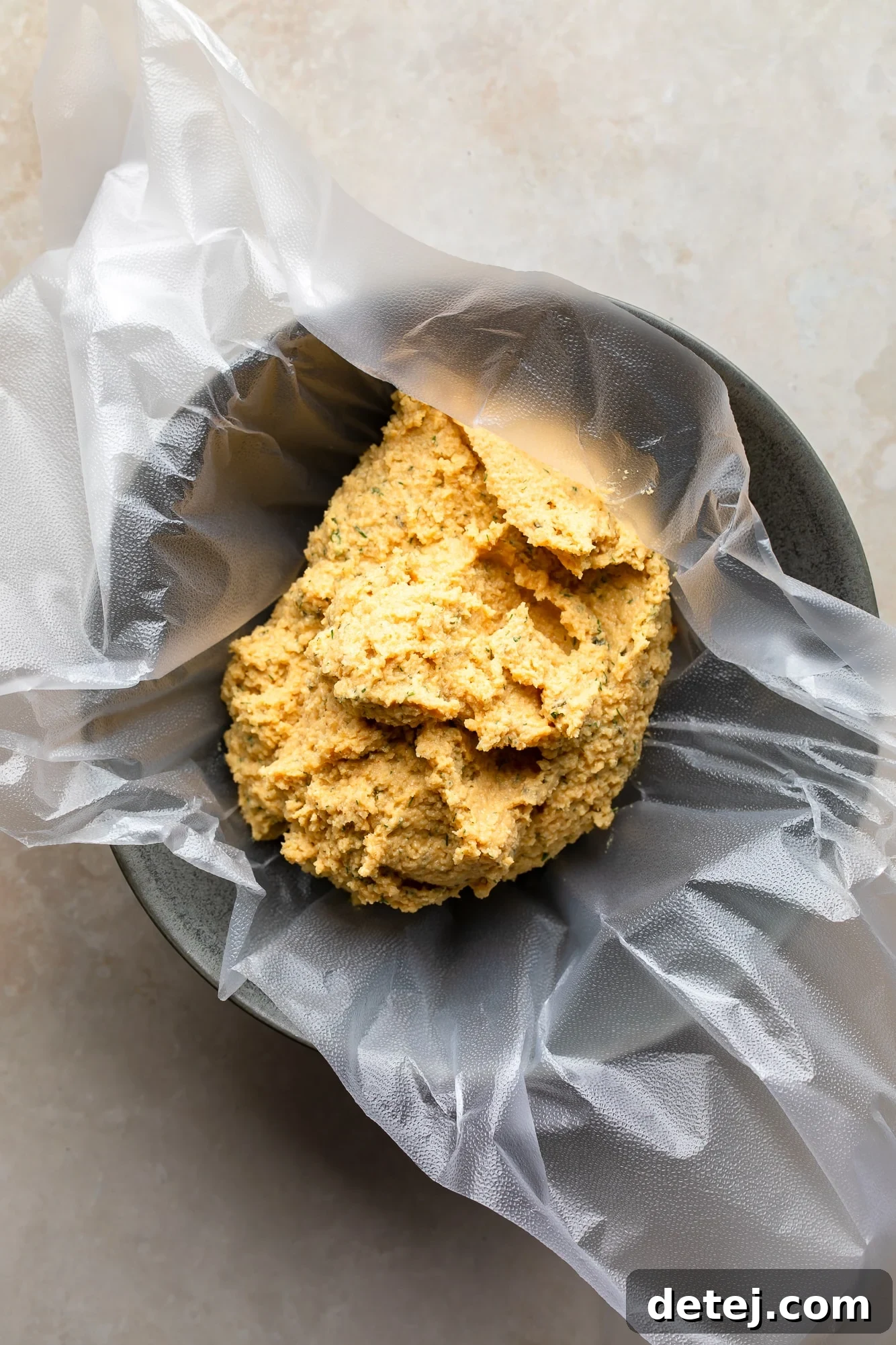 a creamy vegan cheese ball mixture on a sheet of plastic in a small bowl.