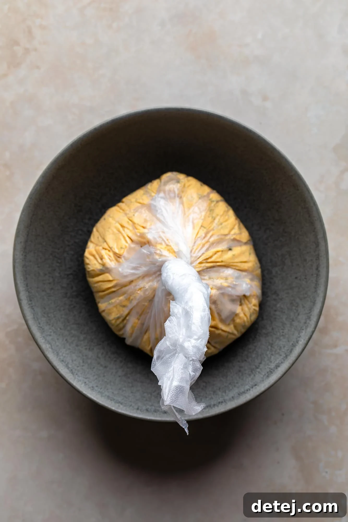 wrapping a creamy vegan cheese ball mixture in a sheet of plastic in a small bowl.