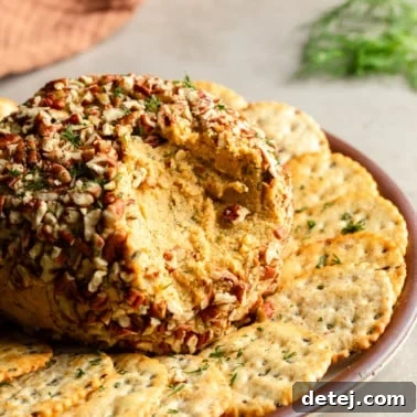a vegan cheese ball with scoop missing on a plate with crackers.