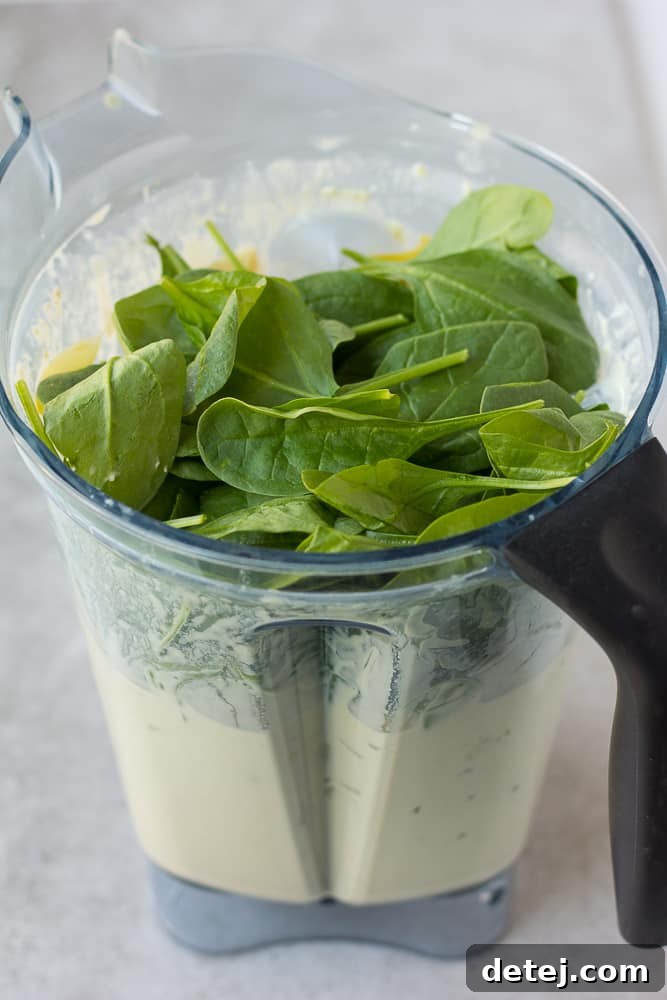Effortlessly Delicious Vegan Spinach Artichoke Dip 5 Fresh spinach and canned artichoke hearts being added to a blender containing the creamy cashew base for a vegan spinach artichoke dip, ready for pulsing.