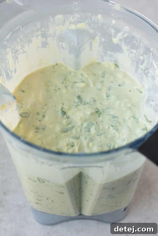 Effortlessly Delicious Vegan Spinach Artichoke Dip 6 A close-up view of the partially blended vegan spinach artichoke dip inside a blender, showing the creamy base mixed with chunky spinach and artichoke pieces before baking.