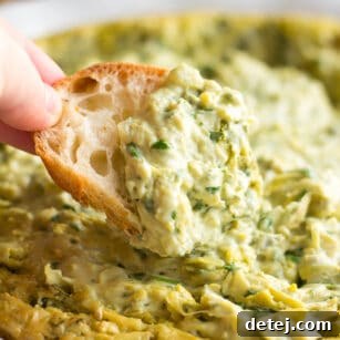 Effortlessly Delicious Vegan Spinach Artichoke Dip 9 A golden brown vegan spinach artichoke dip, served warm with a piece of artisan bread being dipped into its creamy texture.
