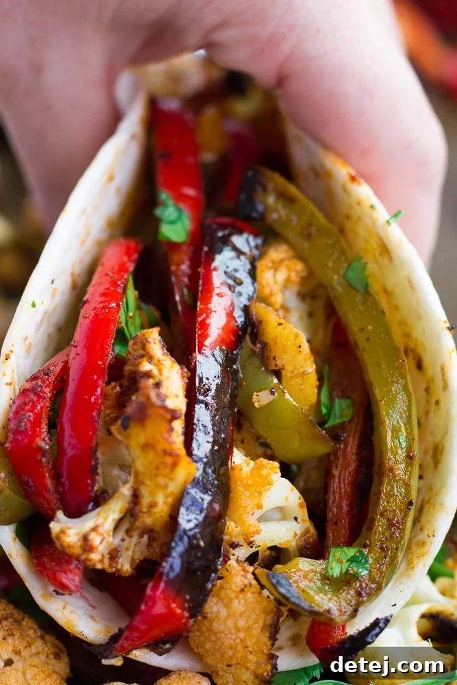 One-Pan Roasted Cauliflower Fajitas 2 A close-up of a warm tortilla generously filled with vibrant, seasoned vegetarian cauliflower fajitas, showcasing the tender cauliflower florets, colorful bell peppers, and caramelized onions.