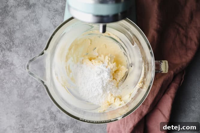 Dreamy Vegan Buttercream 5 Powdered sugar being gradually added to beaten vegan butter in a glass mixing bowl, with the mixer on low speed.