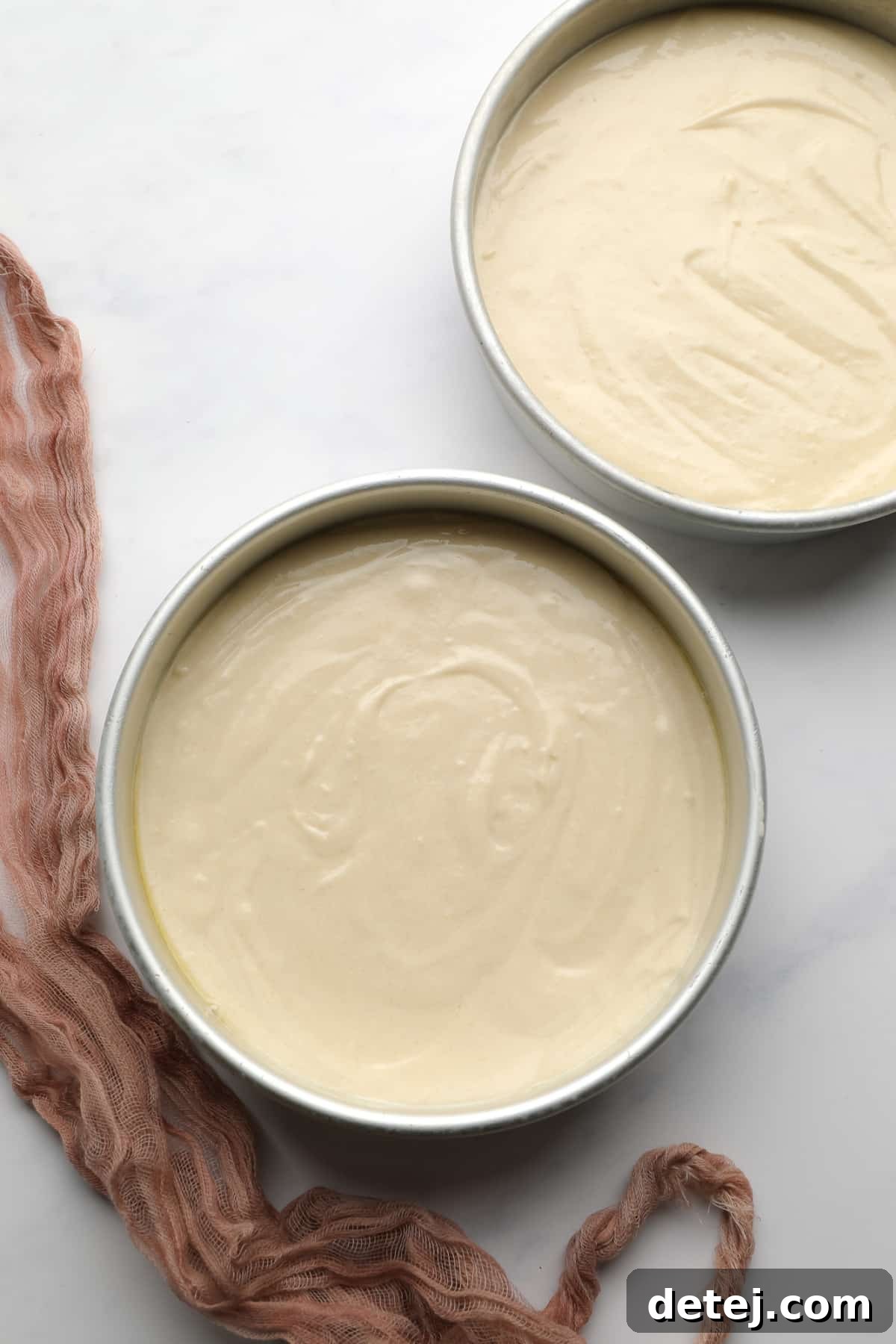 Evenly divided vegan vanilla cake batter filling two round cake pans, ready for baking.