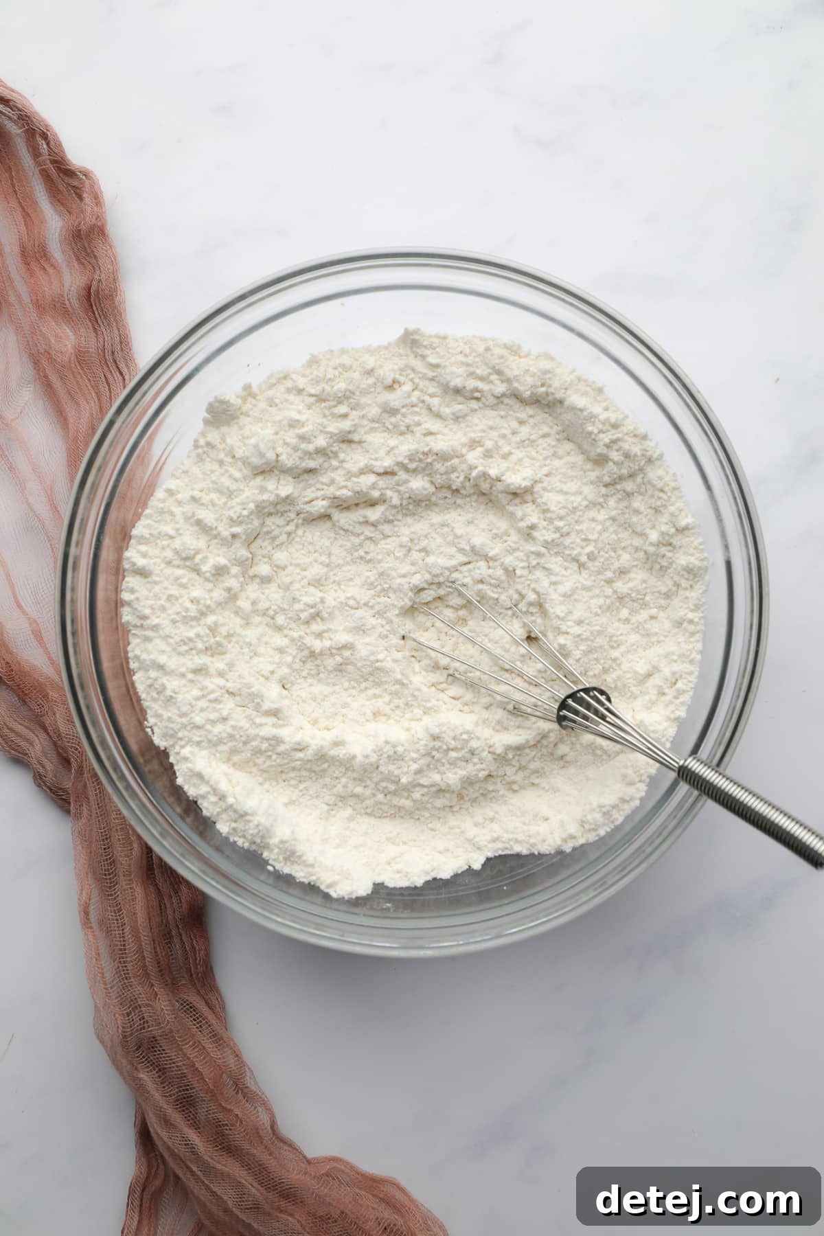 A bowl filled with white flour, baking powder, and salt, ready to be whisked together.