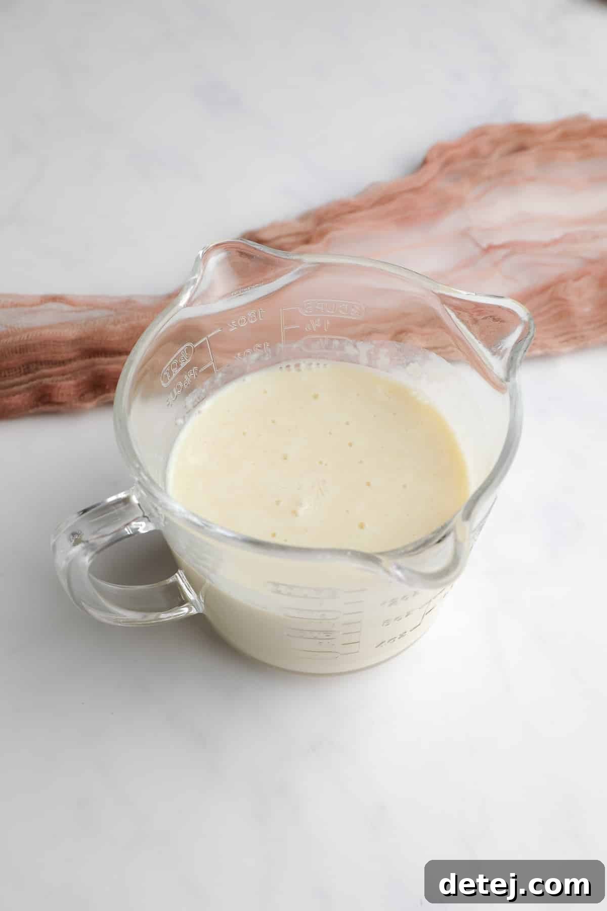 A glass measuring cup containing unsweetened soy milk and apple cider vinegar, beginning to curdle into vegan buttermilk.
