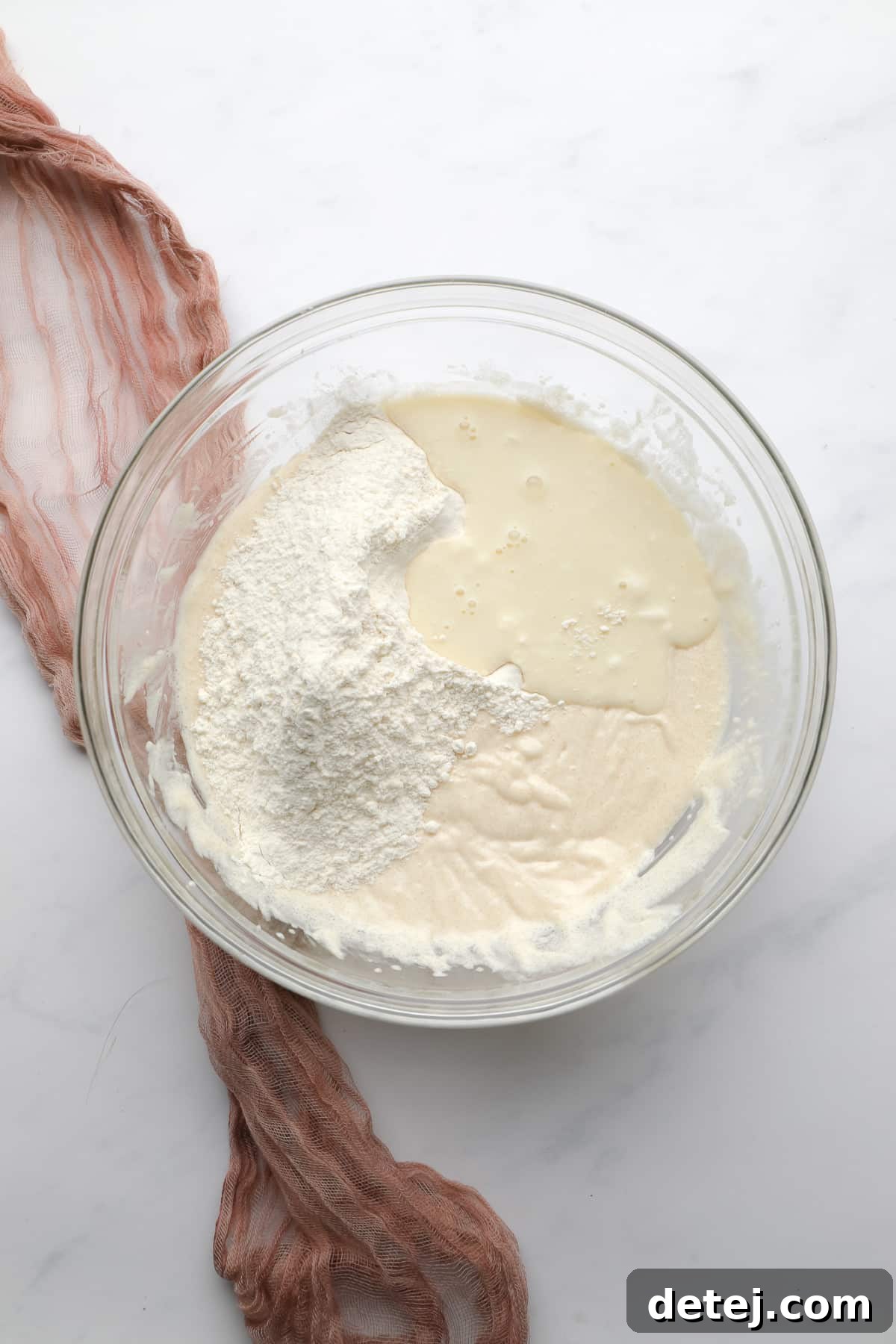 A glass mixing bowl showcasing the process of adding dry flour mixture and vegan buttermilk alternately into the wet batter.