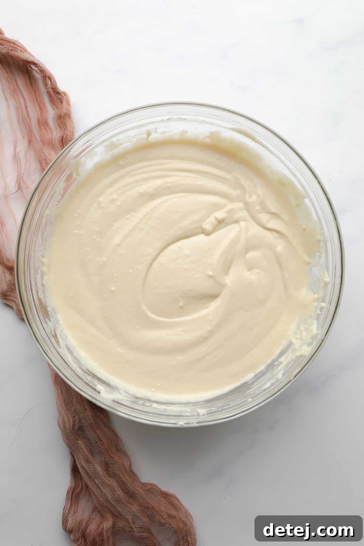The finished vegan vanilla cake batter, a lovely light yellow hue, resting smoothly in a glass mixing bowl.