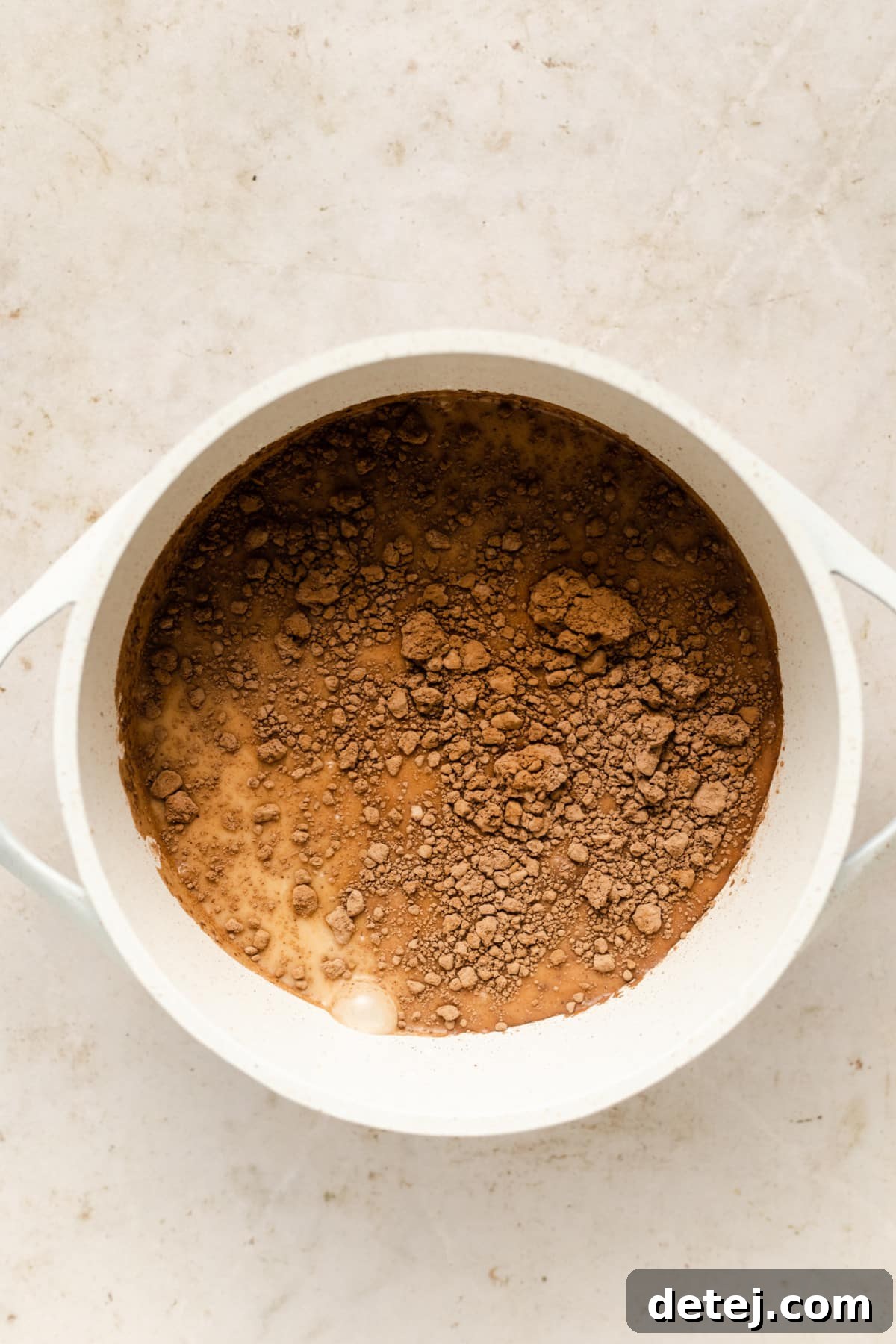 A smooth, dark vegan hot chocolate mixture in a white saucepan on the stove, having just melted and ready for pouring.
