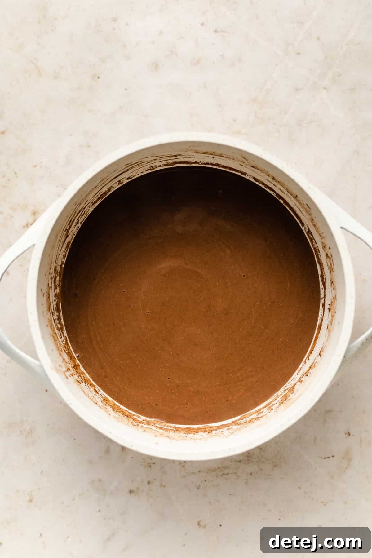A pristine white saucepan filled with rich, dark vegan hot chocolate, perfectly smooth and ready to be served, capturing its inviting texture.
