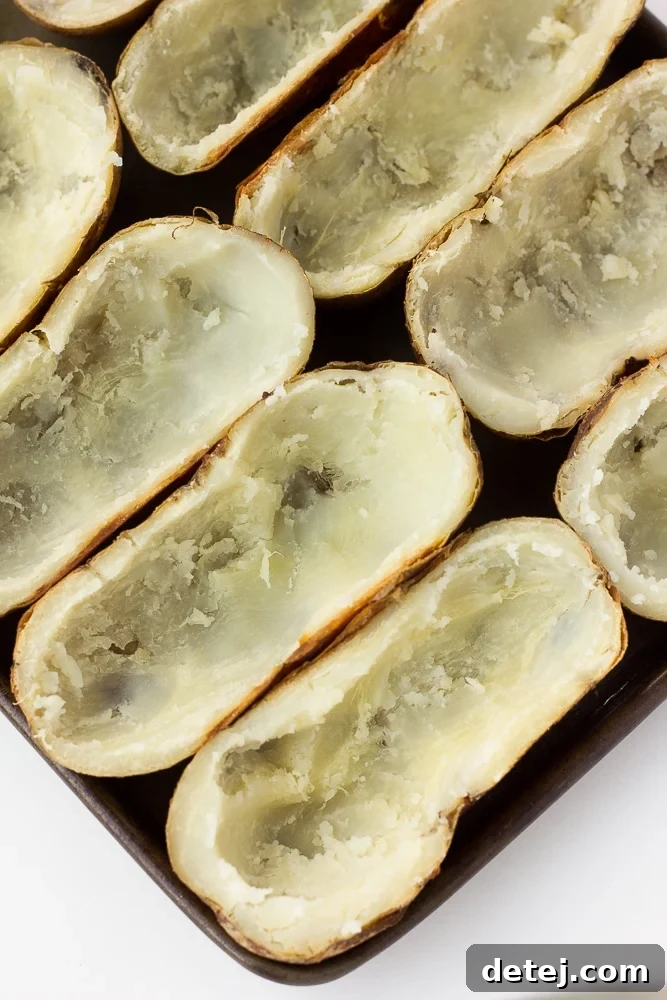 Baked russet potato halves with their fluffy insides carefully scooped out, leaving a sturdy border, arranged on a baking sheet, ready for filling.
