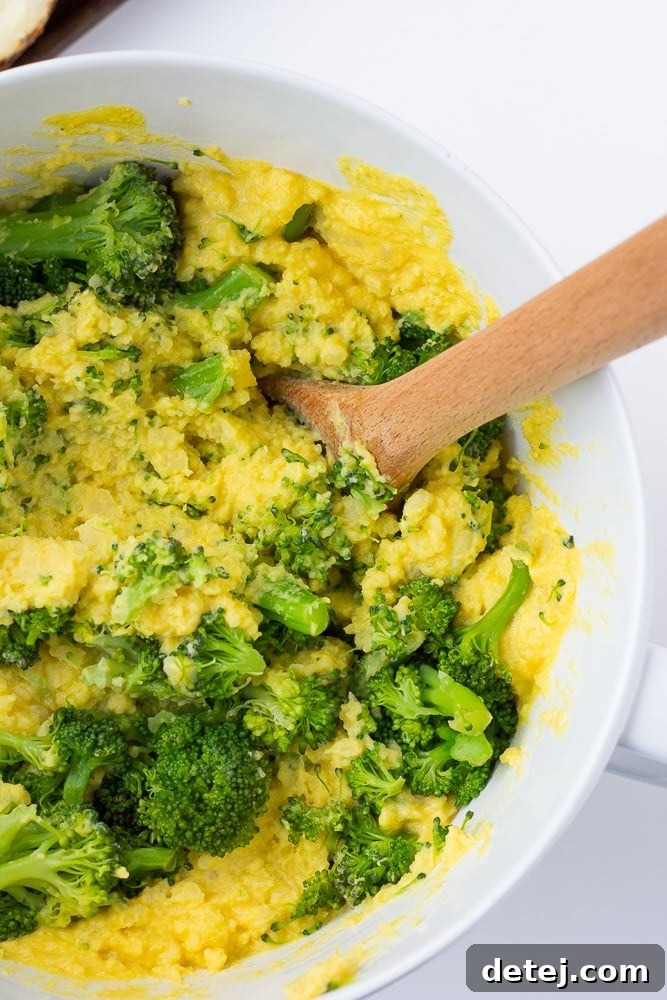 A large mixing bowl filled with creamy mashed potato and vibrant steamed broccoli florets, generously coated in a rich vegan cheese sauce, ready to be scooped back into potato skins.