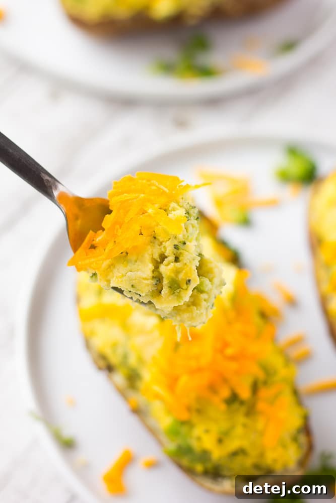 A fork taking a bite from a fluffy, cheesy vegan broccoli twice baked potato, showing the creamy texture and green broccoli pieces within the golden potato skin.