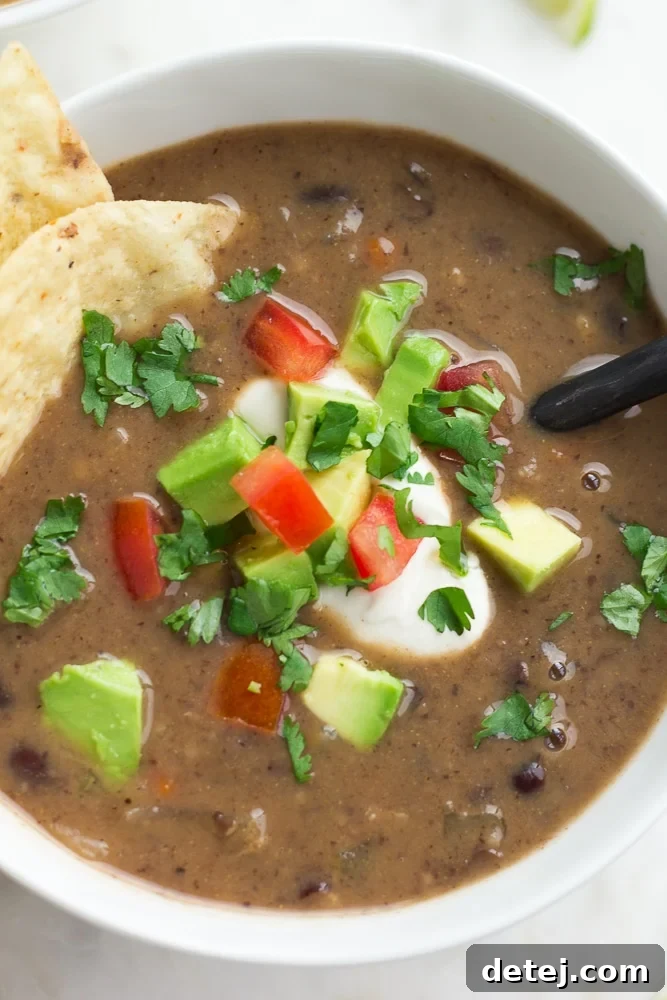 Hearty Vegan Black Bean Soup 5 Close-up of a bowl of creamy vegan black bean soup, topped with vegan sour cream, fresh cilantro, diced tomatoes, and tortilla chips.