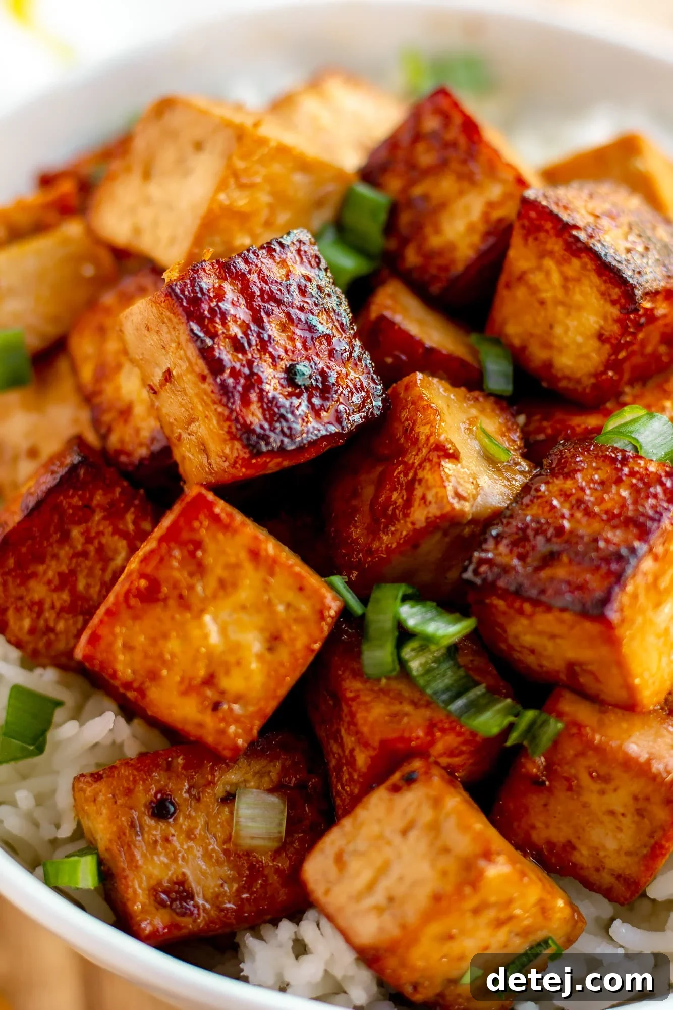 close up on cooked and marinated tofu cubes in a white bowl with rice.