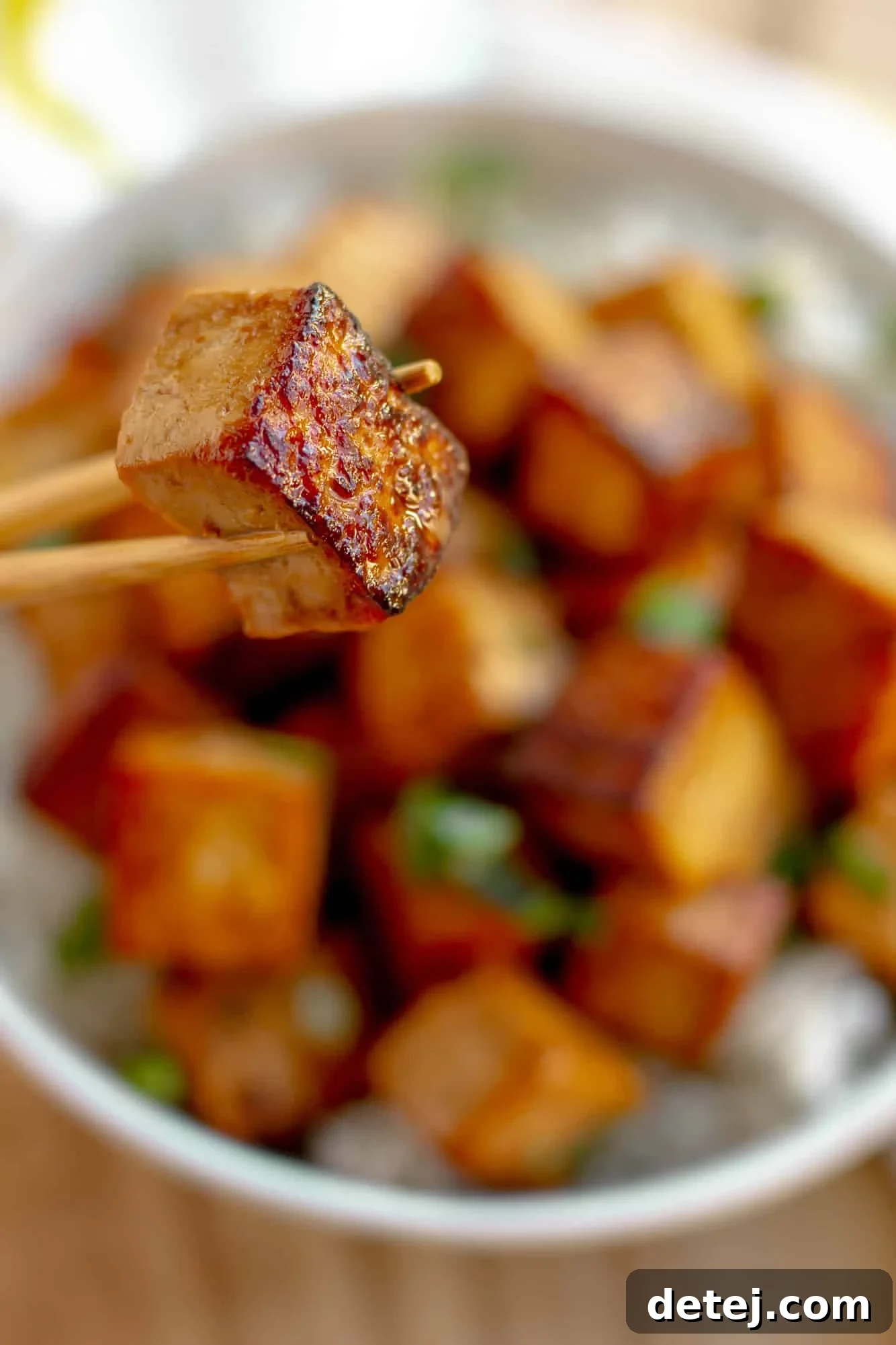 close up on a marinated tofu cube being held up with chopsticks.
