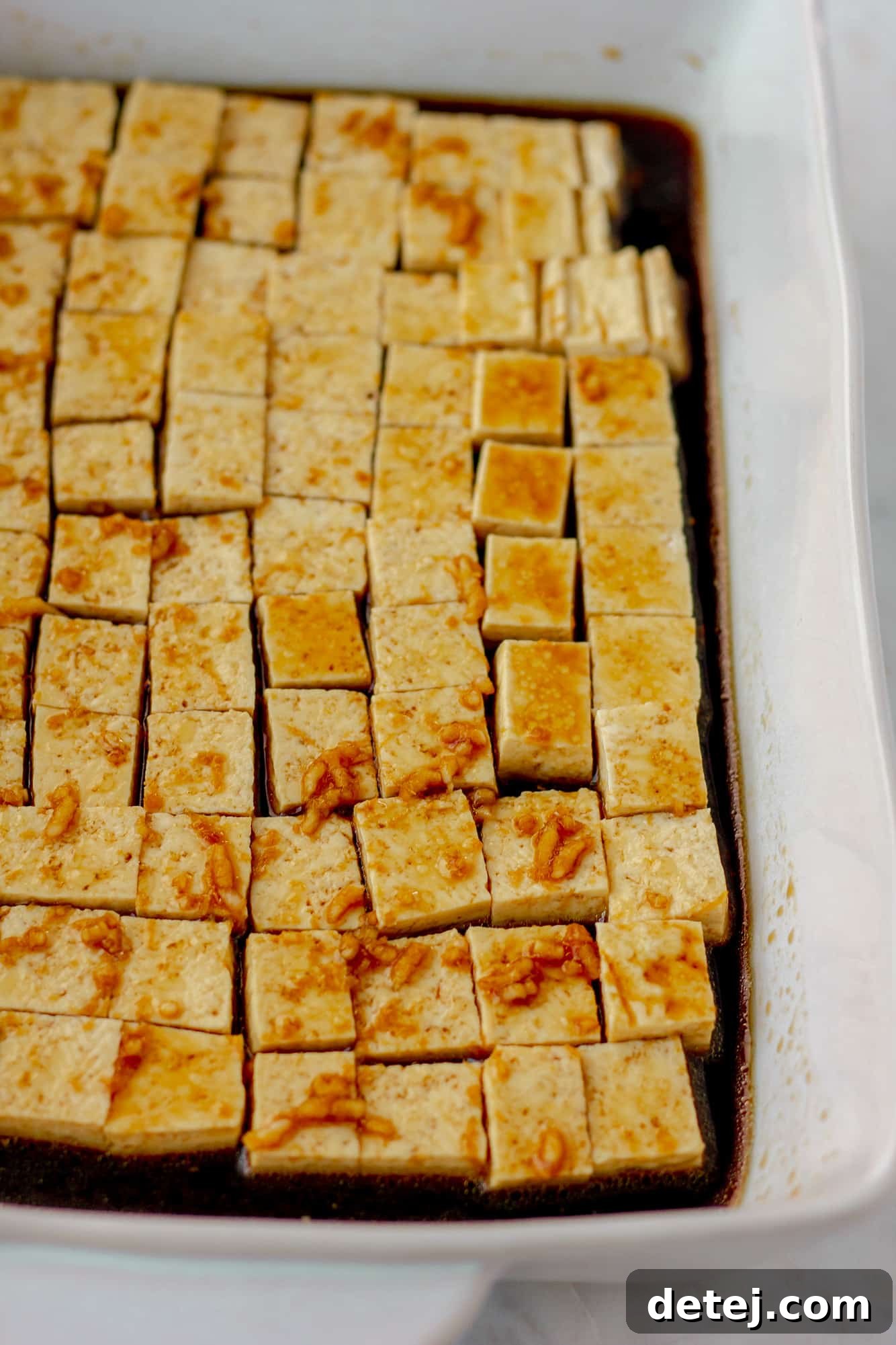 rows of tofu cubes covered in a marinade in a white baking dish.