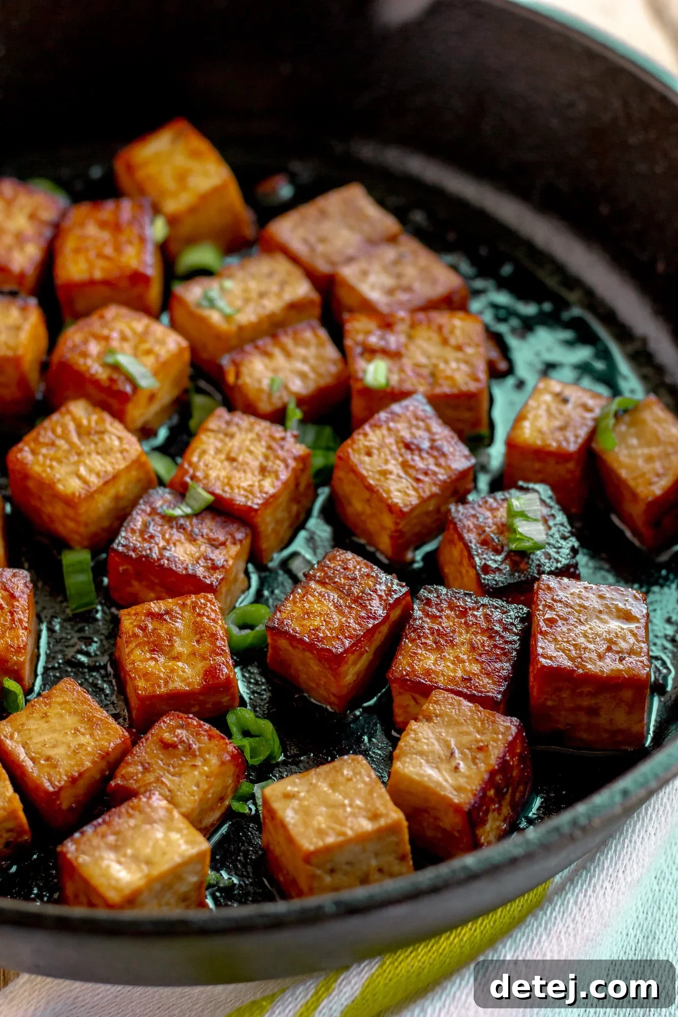 frying marinated tofu cubes in a black skillet.