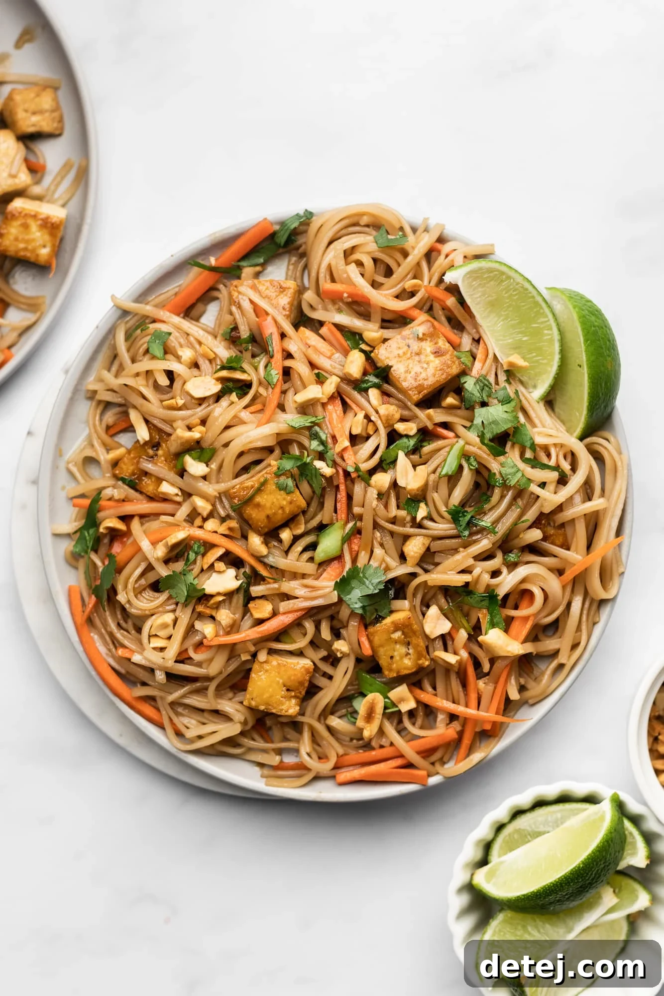 A beautifully plated dish of vegan pad thai, garnished with crushed peanuts, fresh lime wedges, and bright green cilantro.