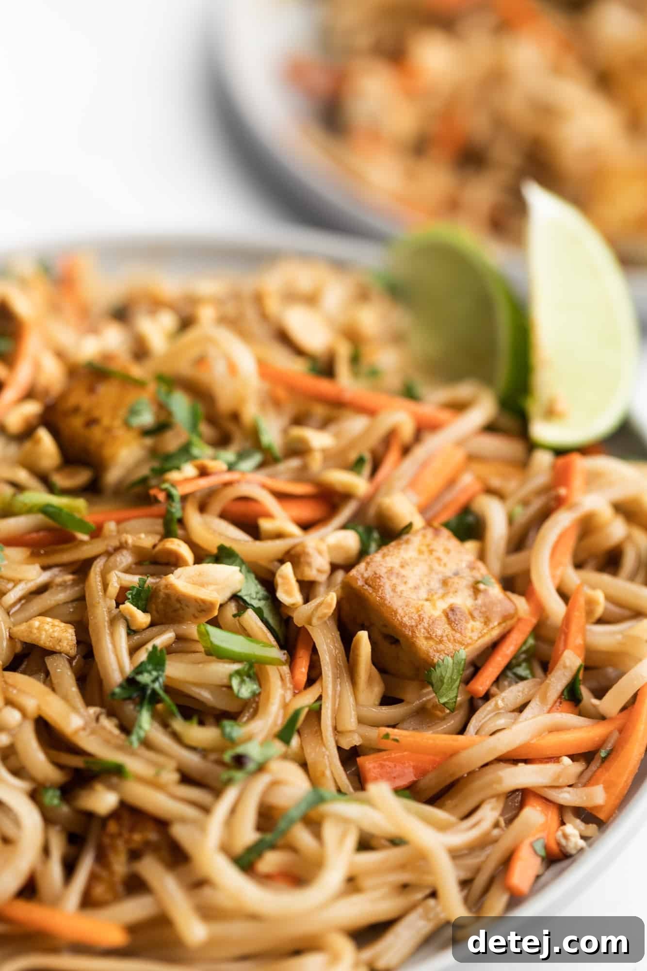A close-up view of vegan pad thai, vibrant with noodles, tofu, and vegetables, adorned with peanuts, lime, and cilantro.