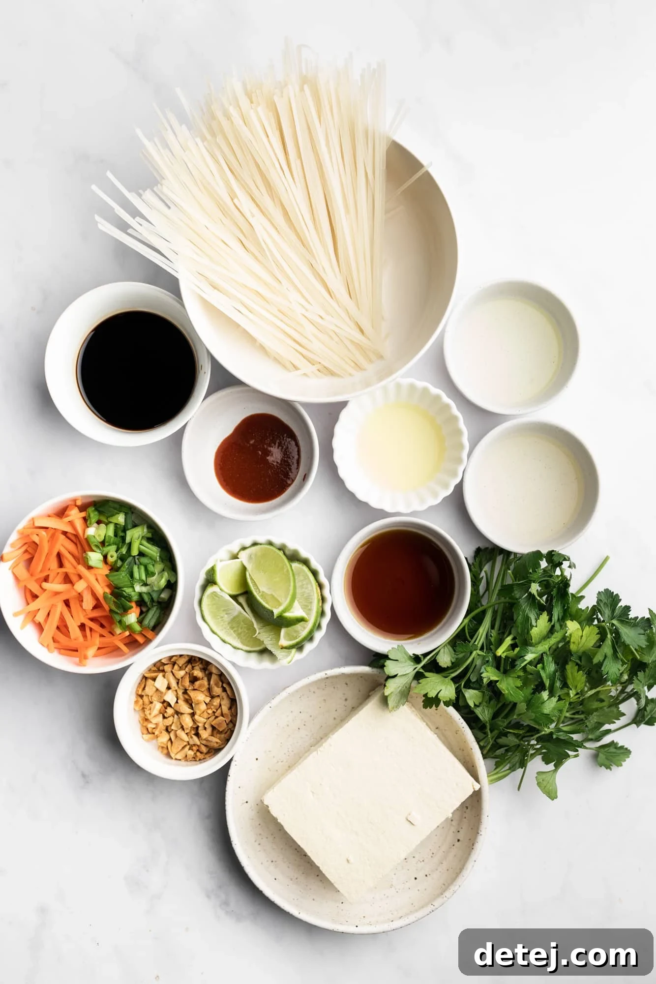 Individual white bowls filled with various ingredients for vegan pad thai, including noodles, tofu, sauce components, and chopped vegetables.