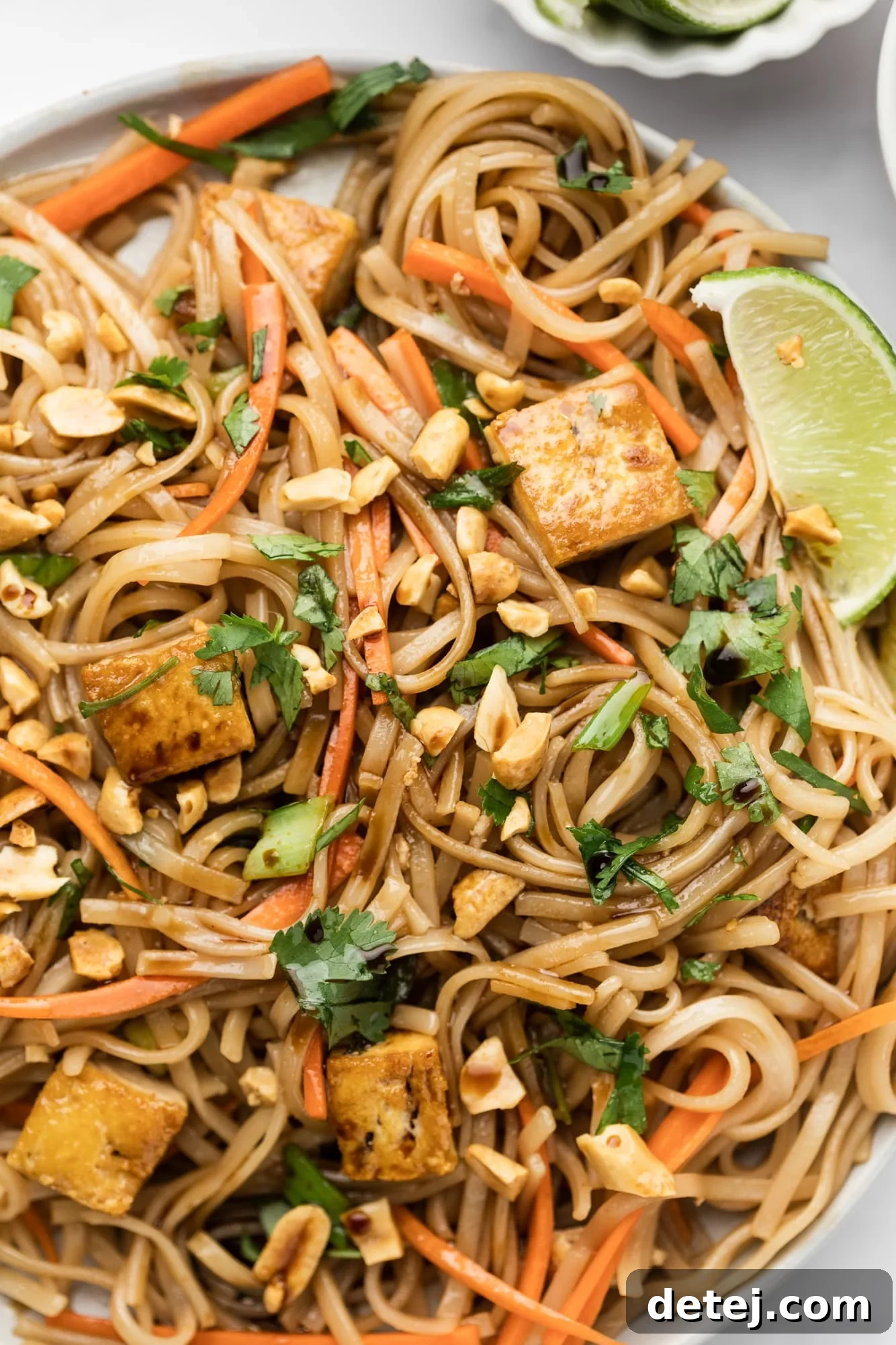 A close-up shot of the finished vegan pad thai dish, elegantly topped with crushed peanuts, fresh lime wedges, and green cilantro leaves.