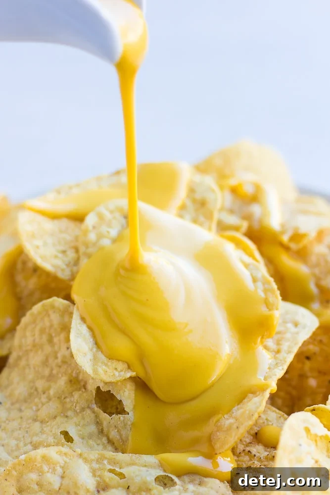 Rich, golden vegan cheese sauce being generously poured over crispy tortilla chips, creating a perfect stack for ultimate nachos. This all-purpose, nut-free plant-based sauce is also ideal for baked potatoes or steamed broccoli.